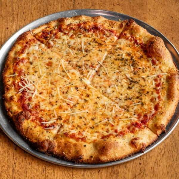 A whole cheese pizza with red sauce and herbs, sliced on a metal pan.