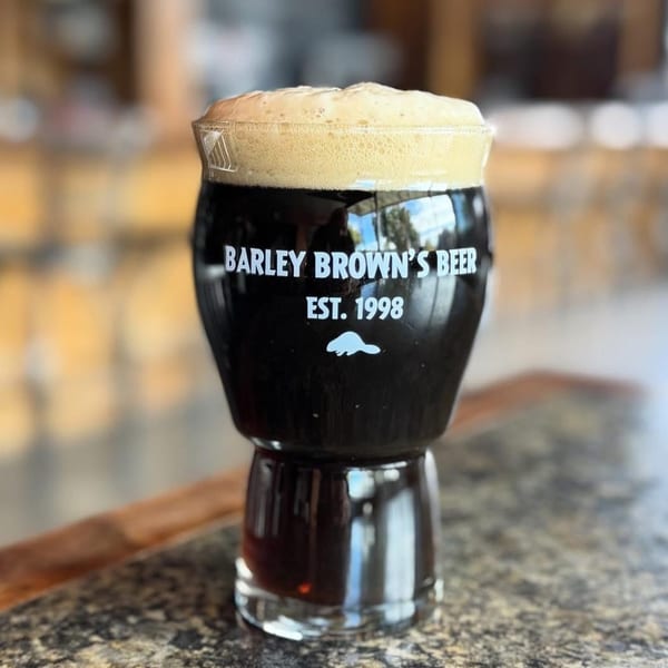 A glass of dark Barley Brown's Beer with a foamy head sits on a counter.